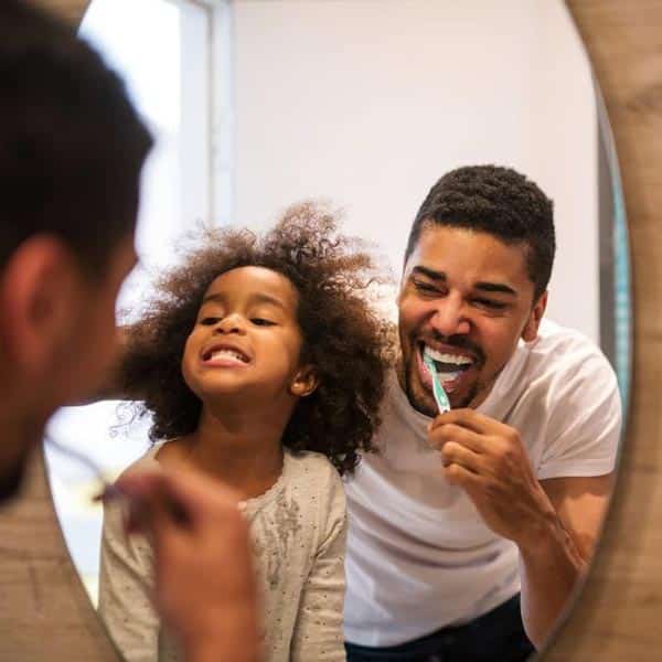 father and daughter brushing teeth in mirror